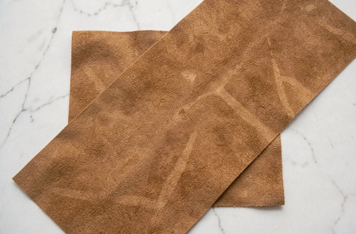 Gros plan sur un tissu en daim caramel posé sur marbre blanc, révélant la texture veloutée et les nuances naturelles du matériau